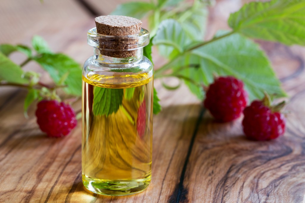 A bottle of raspberry seed oil with fresh raspberries in the background